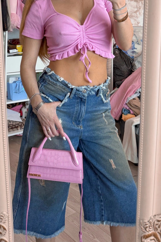 Model purtând bermude oversized din denim albastru cu talie joasă și aspect distressed.