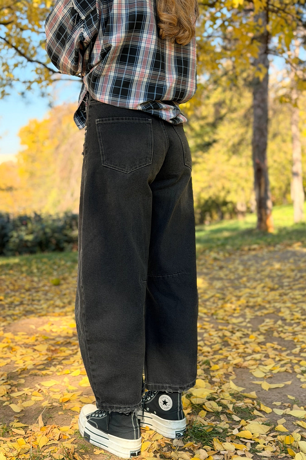 Vedere din spate a blugilor damă tip balon negri, croi lejer și purtați cu cămașă în carouri