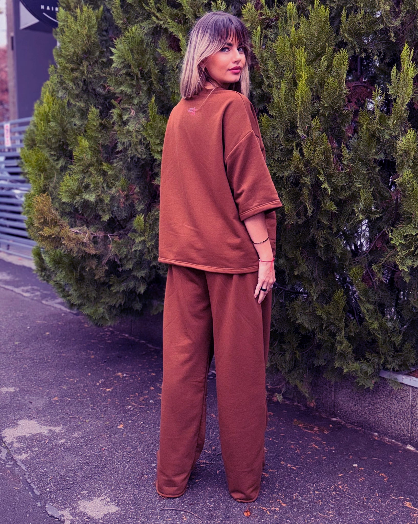 Trening damă maro din două piese, capturat din spate, cu bluză oversize și pantaloni lejeri